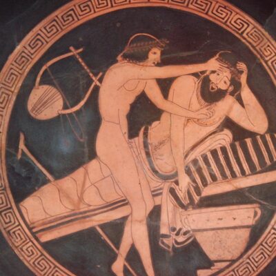 A servant holds the head of a symposium guest about to vomit into his skyphos.